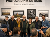 Seven photographers standing in front of framed photos at an exhibition titled Photographers of the North