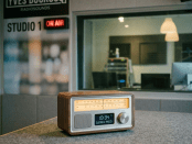 Radio host speaking into microphone in sound studio with mixing console and computer screen